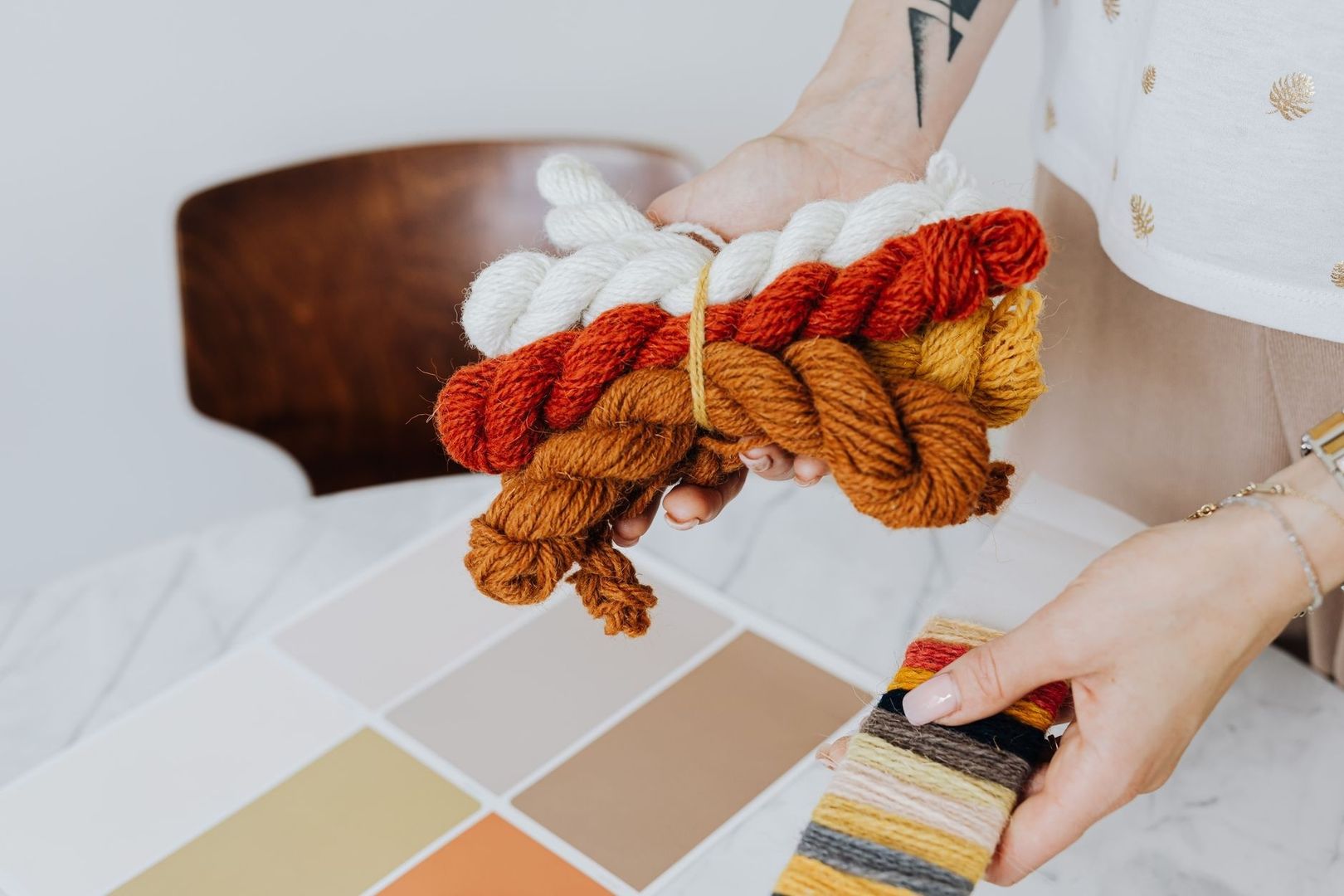 Hands holding colorful yarn skeins beside a palette of earthy color swatches