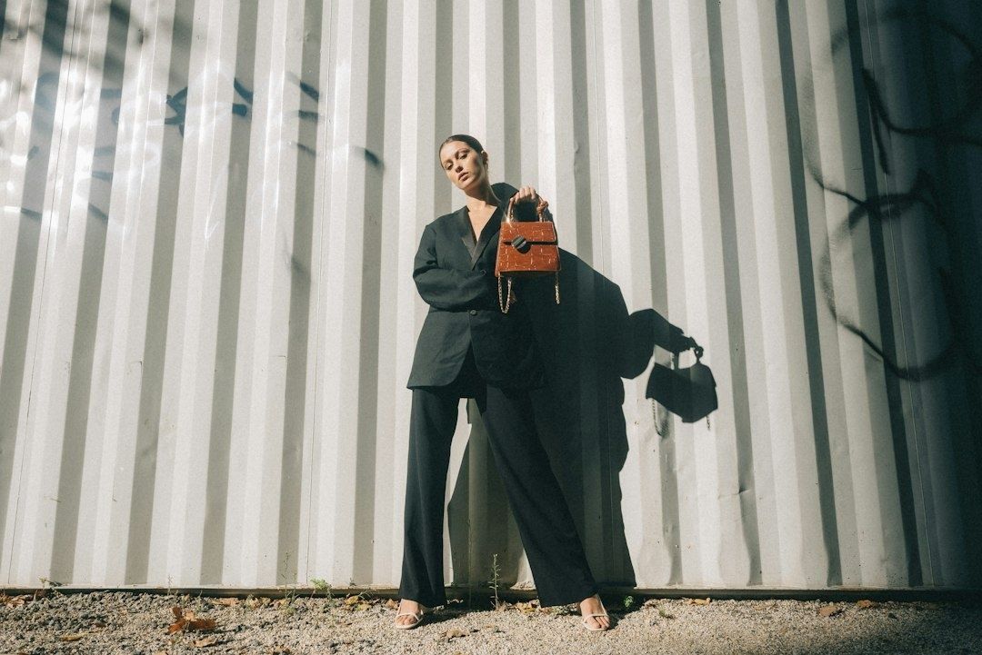 Person in oversized black suit holding a structured brown handbag